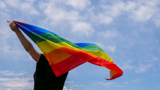 Bisexuelle lesbische transgenderfrau steht an einem sonnigen tag mit lgbt-flagge gegen blauen himmel mit wolken