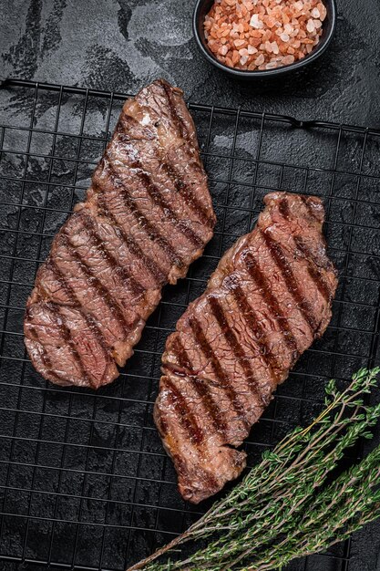 Foto bistec de carne de res a la parrilla en un estante de fondo negro vista de arriba