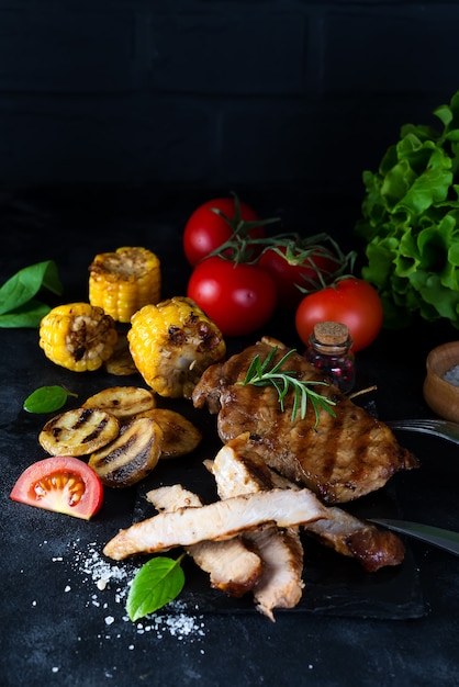 Bistec de cerdo a la parrilla y verduras, papas al horno y ensalada verde en oscuridad