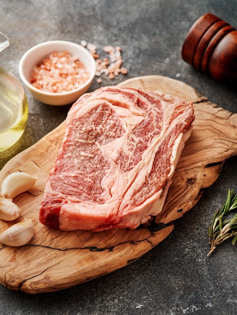 Bistec de chuletón crudo en una tabla de madera Preparando bistec de ternera crudo para parrilla