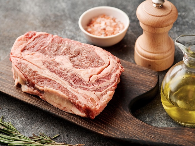 Bistec de chuletón crudo en una tabla de madera Preparando bistec de ternera crudo para parrilla