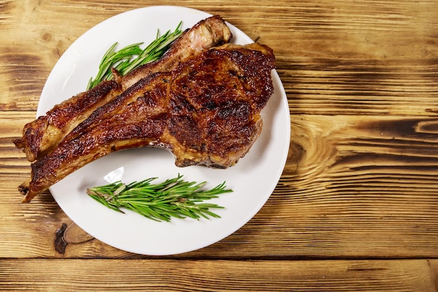 Bistec de costilla de ternera asada sobre hueso con romero en plato blanco sobre mesa de madera