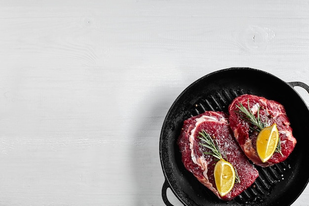 Bistec crudo en una sartén a la parrilla con hierbas y aceite en el lugar de la vista superior de fondo blanco para el texto