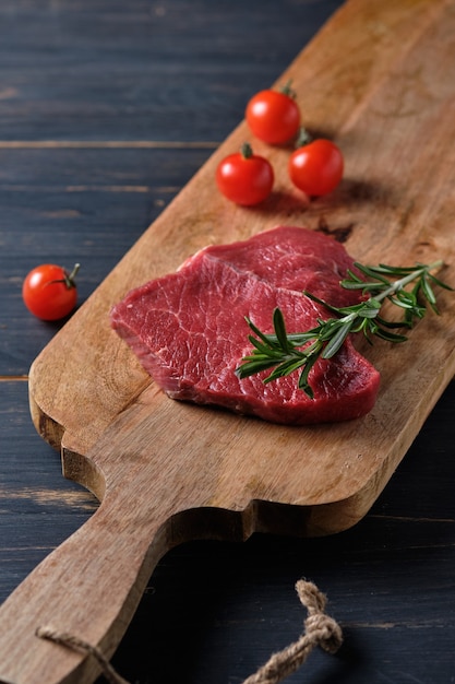 Bistec crudo sobre una tabla de madera, adornado con tomates cherry y una ramita de romero.