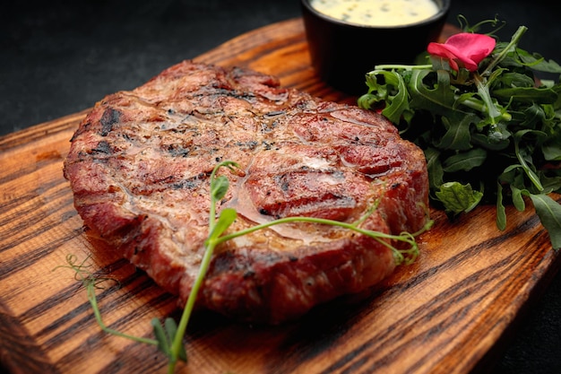 Bistec de cuello de cerdo con salsa y rúcula sobre una tabla de madera