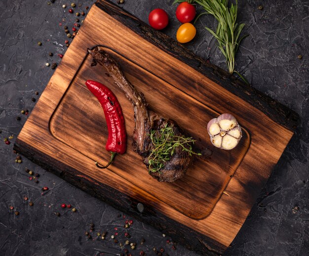 Bistec jugoso americano en el tablero con especias, tomate y verduras a la parrilla. Sobre una mesa negra