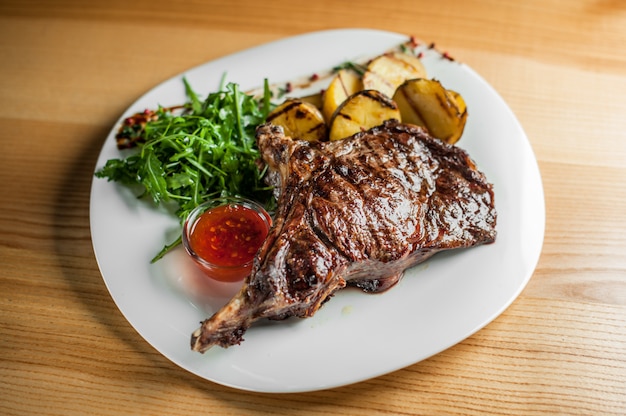 Un bistec jugoso y apetitoso, cocinado a la parrilla con verduras y salsa en un plato blanco.