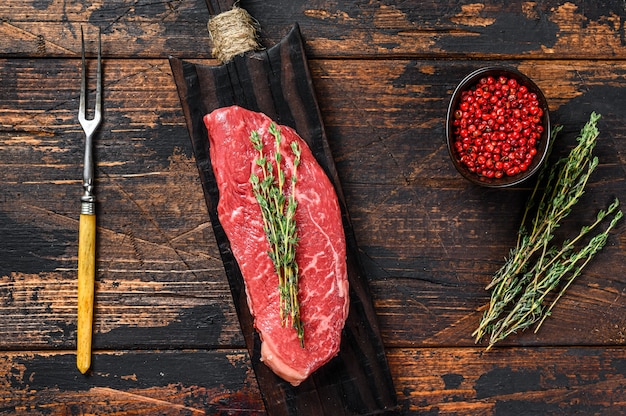 Bistec de lomo crudo sobre una tabla de cortar, carne de vacuno veteada Fondo de madera oscura. Vista superior.