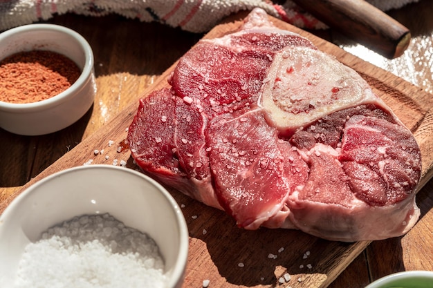 Un bistec de ossobuco de carne cruda fresca en un tablero con guarniciones en una mesa de madera Concepto de proteína animal Comida italiana Vista aérea