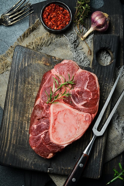 bistec de ossobuco crudo con romero y especias sobre un fondo de piedra negra Espacio libre para el texto