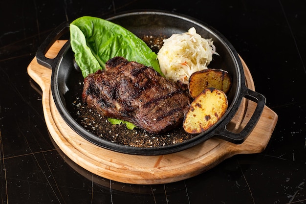 Bistec a la parrilla con papas doradas al horno servidas con repollo agrio y salsa roja sobre un fondo oscuro Receta deliciosa Filete de cerdo cocinado en sartén para la cena Textura de carne frita jugosa