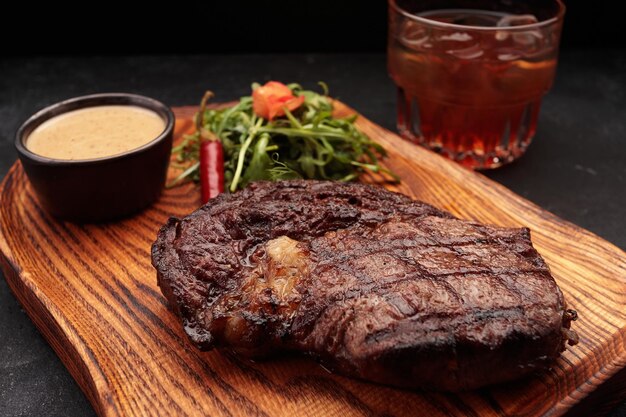 Bistec a la parrilla con salsa de hierbas y un vaso de whisky en una tabla de madera