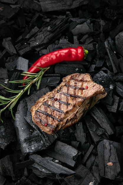 Foto bistec a la parrilla sobre un fondo de carbón negro