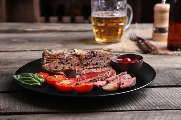 Bistec a la parrilla con tomates en plato y jarra de cerveza en mesa de madera