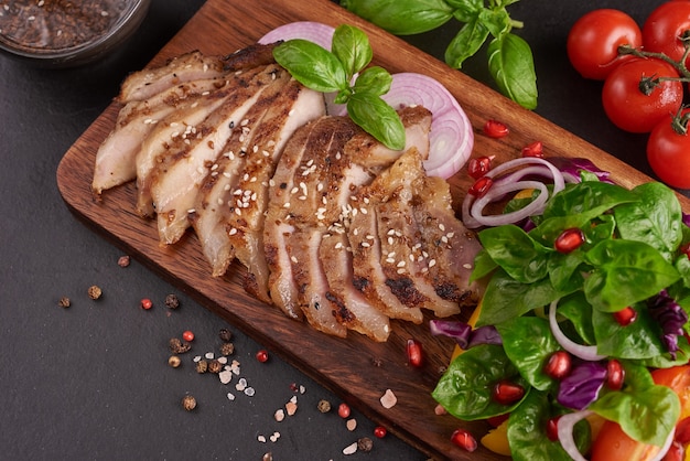 Bistec a la parrilla con verdura fresca, pimiento dulce, tomate, cebolla morada, pimiento rosa y especias. Comida sabrosa casera. Concepto de comida sabrosa y saludable. Superficie de piedra negra. Filete de cerdo con ensalada