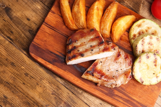 Foto bistec a la parrilla verduras a la par rilla y piezas de patatas fritas en tabla de madera sobre fondo de mesa