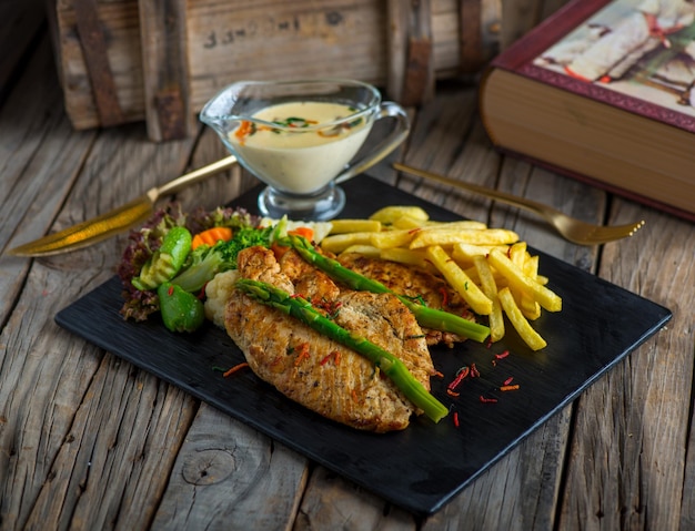 Bistec de pollo con papas fritas aislado en una tabla de cortar en la vista lateral de fondo de madera del bistec