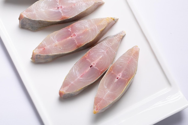 Bistec de Pomfret crudo dispuesto en un plato de cerámica en forma de rectángulo plano con fondo blanco.