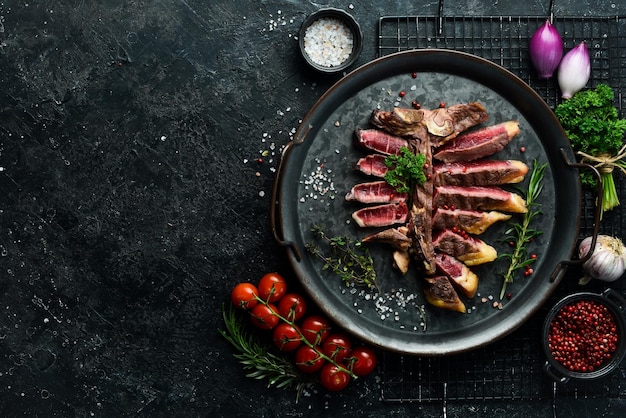 Bistec de porterhouse jugoso picado o bistec T Bone seco de ternera envejecida Listo para cocinar en una tabla de madera con hierbas, pimienta y sal Sobre un fondo de piedra negra