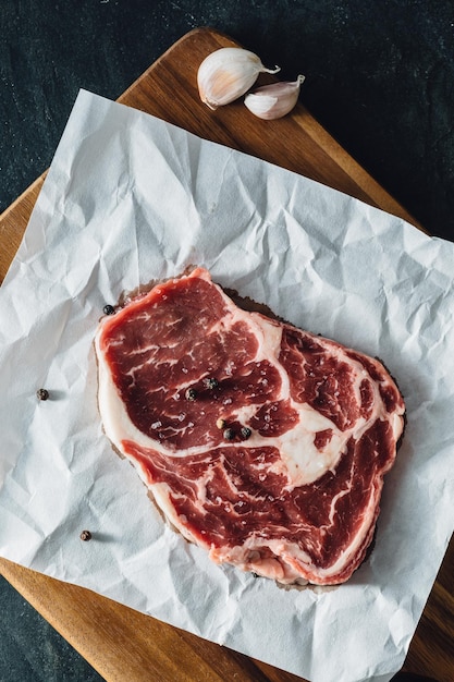 Foto bistec de ribeye con tabla de cortar de madera sobre un fondo negro de piedra