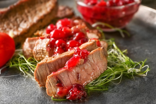 Bistec en rodajas servido con salsa de arándanos en placa de metal