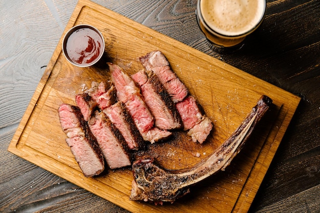 Bistec de solomillo de ternera marmolada Bistec de Nueva York sobre una tabla de madera con un vaso de cerveza oscura y salsa barbacoa