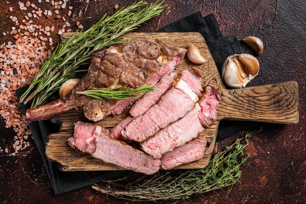 Bistec Tomahawk asado a la barbacoa, ojo de costilla en una tabla de madera. fondo oscuro Vista superior.