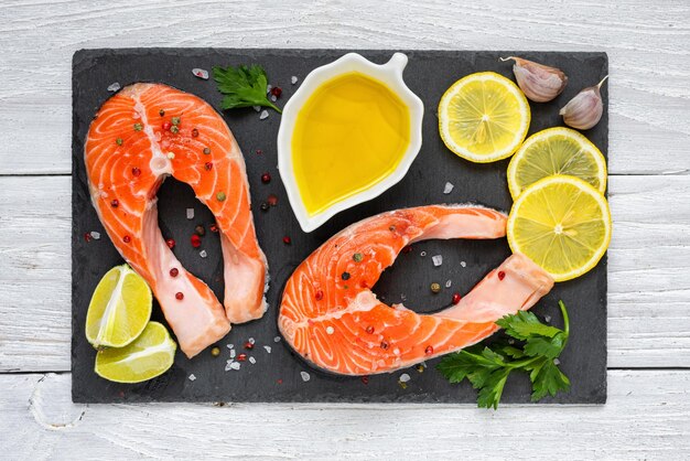 Foto bistecs de salmón con limón y especias en tablero de pizarra negra en mesa de madera blanca pescado rico en omega