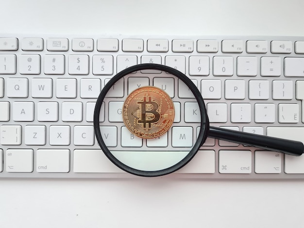Bitcoin ausstehende Lupe und Bitcoin-Münze auf weißer Computertastatur