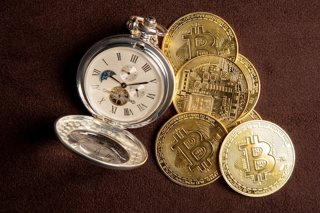 Bitcoin-Bitcoin-Münzen und eine Vintage-Taschenuhr auf einer Draufsicht aus braunem Lederhintergrund