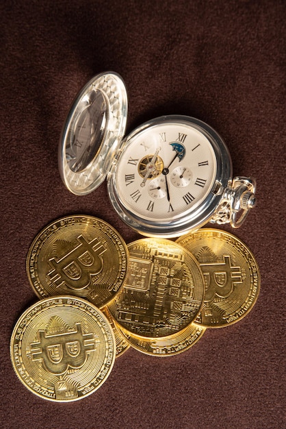 Bitcoin-Bitcoin-Münzen und eine Vintage-Taschenuhr auf einer Draufsicht aus braunem Lederhintergrund