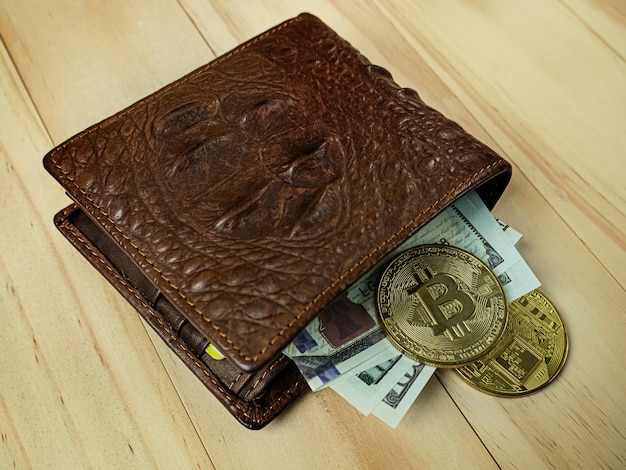 El bitcoin en cartera de piel de cocodrilo sobre mesa de madera.