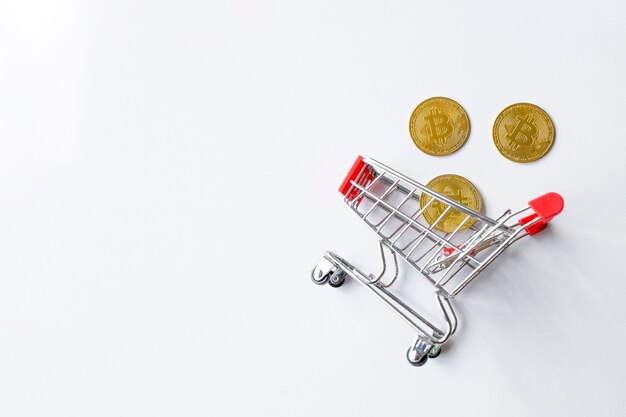 Bitcoin dorado en carrito de compras sobre fondo blanco de mesa. vista superior