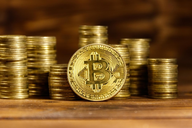 Bitcoin dorado y pilas de monedas sobre fondo de madera