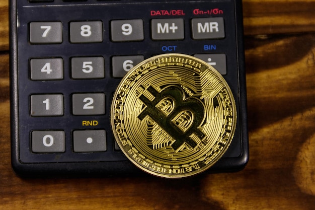 Bitcoin dourado e calculadora na mesa de madeira