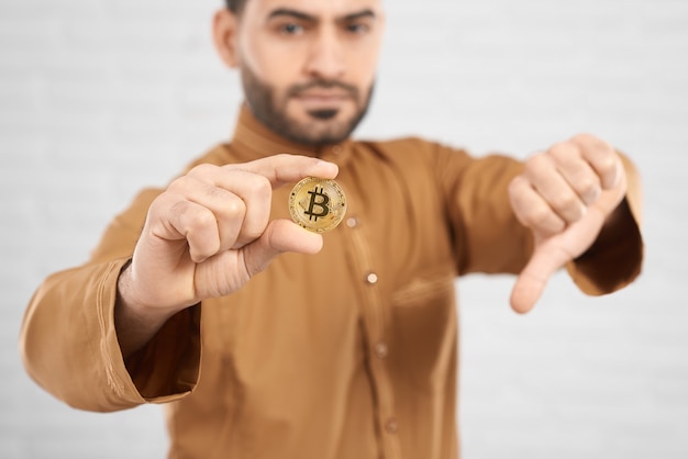 Bitcoin dourado espera pelo modelo masculino muçulmano atraente, mostrando os polegares para baixo