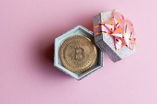 Bitcoin se encuentra en una pequeña caja de regalo en el fondo de color rosa.