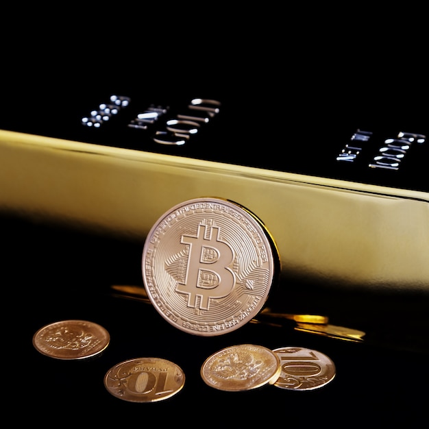 Bitcoin-Kryptowährung und Goldbarren auf einem schwarzen Feld.