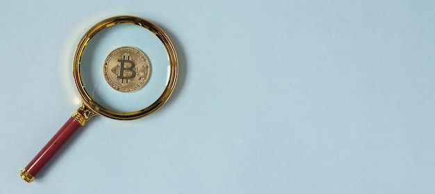 Bitcoin-Münze durch Lupe auf blauem Hintergrund