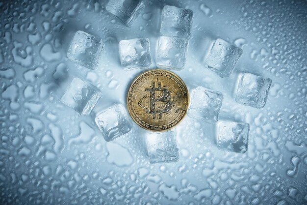 Bitcoin-Münze schmelzende Eiswürfel und Wassertropfen auf hellem Hintergrund.