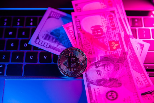 Bitcoin-Münze und US-Dollar in Neon auf Laptop-Tastatur-Kryptowährungs-Investitionskonzept