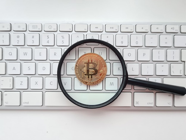 Bitcoin pendiente lupa y moneda bitcoin en teclado de computadora blanco