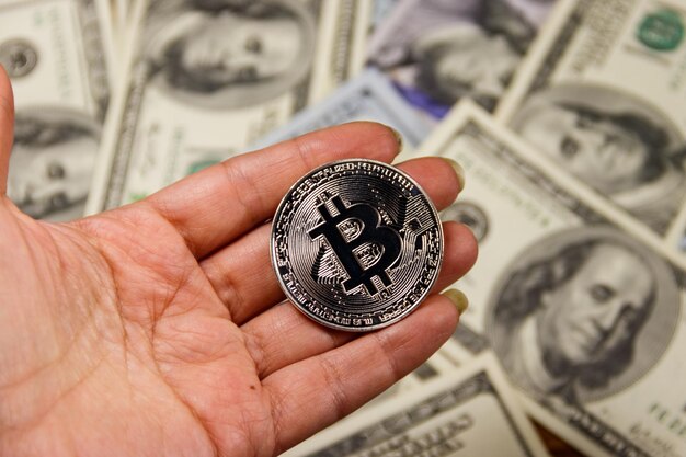 Bitcoin de plata en la mano contra billetes de cien dólares