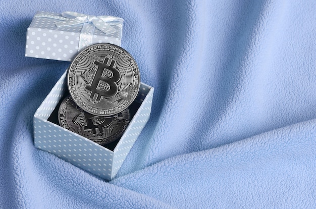 El bitcoin plateado se encuentra en una pequeña caja de regalo azul con un pequeño lazo.