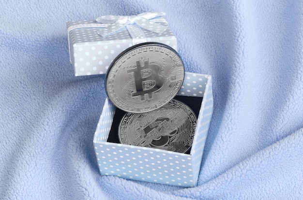 El bitcoin plateado se encuentra en una pequeña caja de regalo azul con un pequeño lazo.