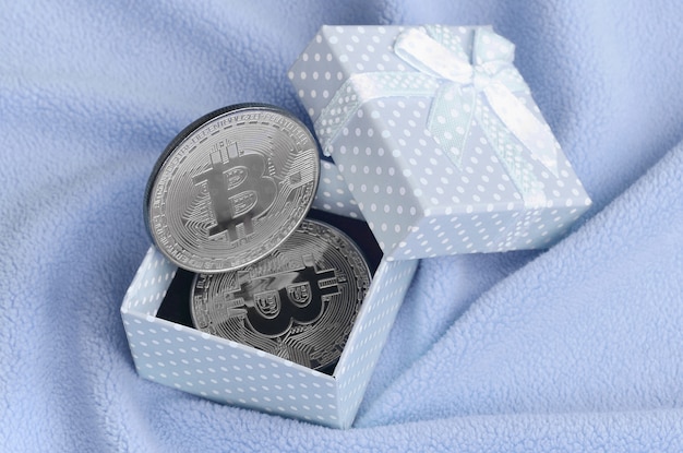 El bitcoin plateado se encuentra en una pequeña caja de regalo azul con un pequeño lazo.