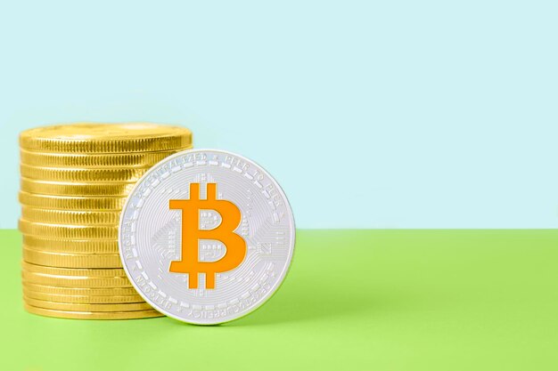 Bitcoin plateado con un símbolo dorado junto a una pila de monedas de oro sobre un fondo brillante de dos tonos Ahorro e intercambio de dinero en concepto de criptomoneda con espacio de copia Antecedentes comerciales financieros