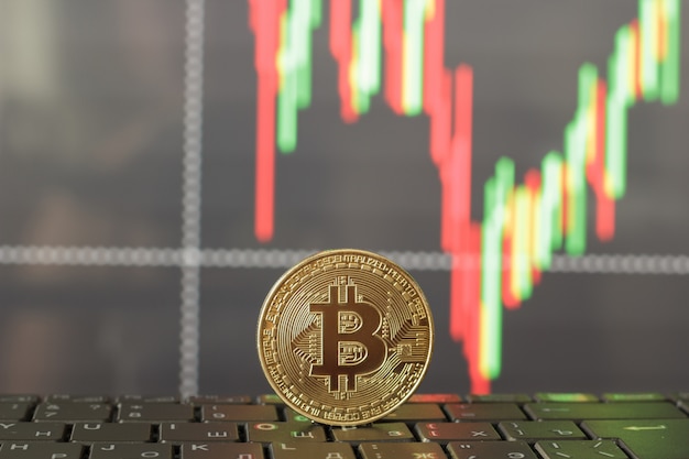 Un bitcoin en el teclado y una gráfica del crecimiento y caída de los precios.