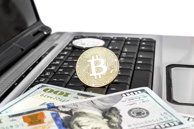 Bitcoins de metal com notas de dólar no laptop em fundo branco Conceito de negócios