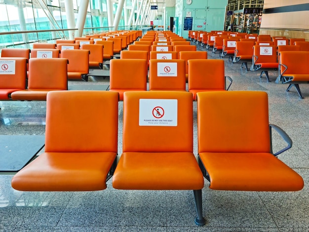 Bitte benutzen Sie diesen Sitzplatz nicht Soziale Distanz an Flughäfen und Bahnhöfen Leerer Flughafen mit Sitzplätzen